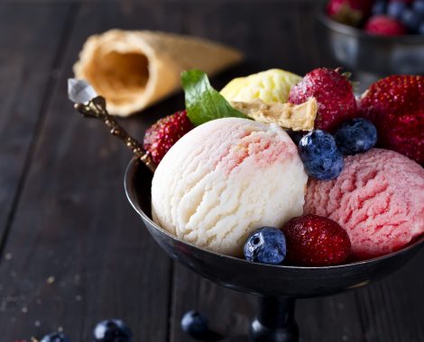 Bowl with ice cream with three different scoops of white, yellow, red colors and waffle cone with frozen berry on dark wooden background , copy space